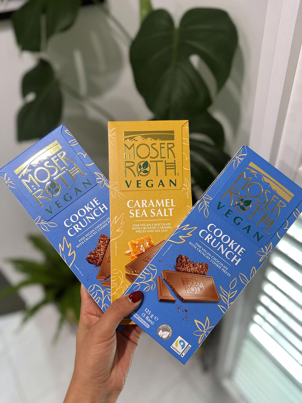 A hands three blocks of the Moser Roth vegan range. Two blocks of vegan cookie crunch chocolate and one vegan caramel sea salt.