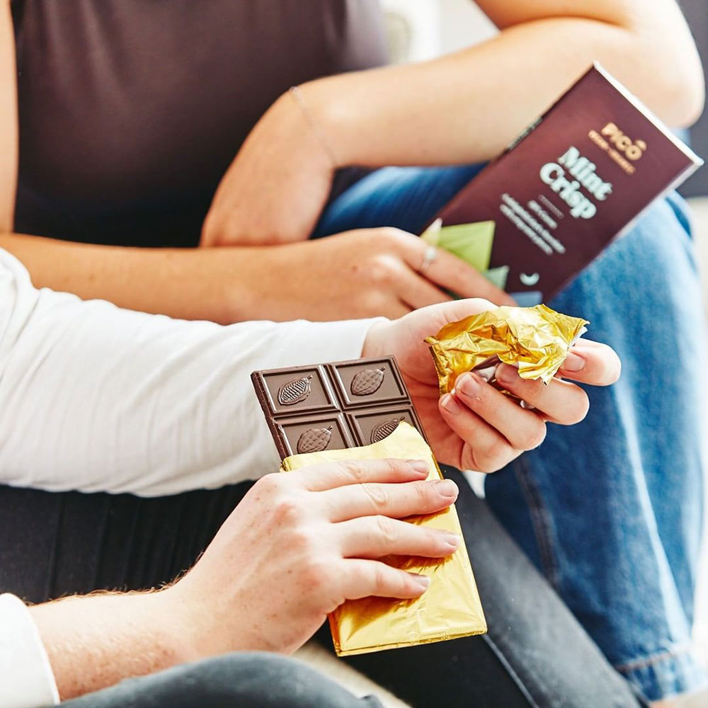 Two people are sitting down outside, both holding blocks of Pico chocolate.