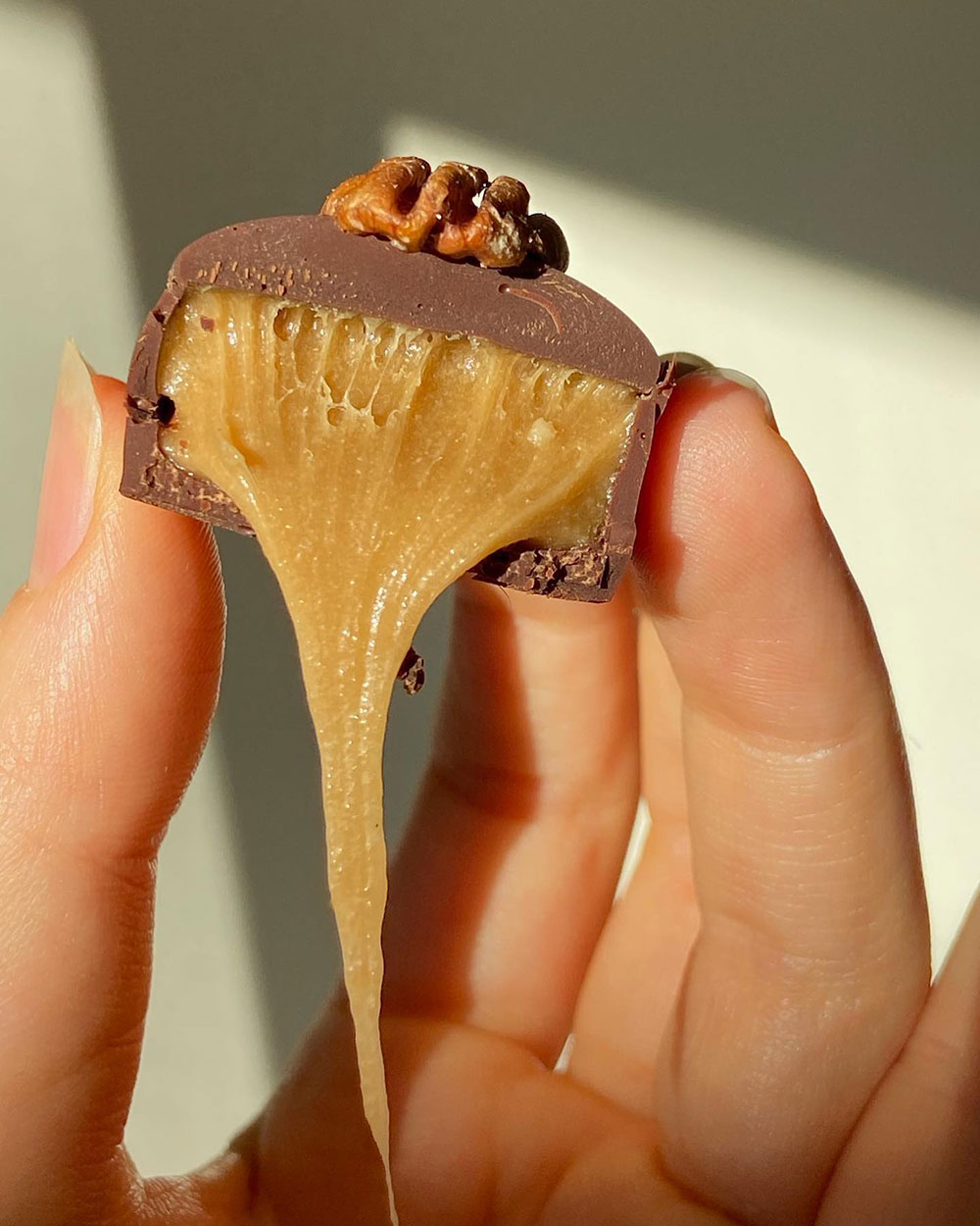 A hand hold up a cross section of a Butter Caramel Pecan Truffle by Loco Love. Caramel is oozing out.