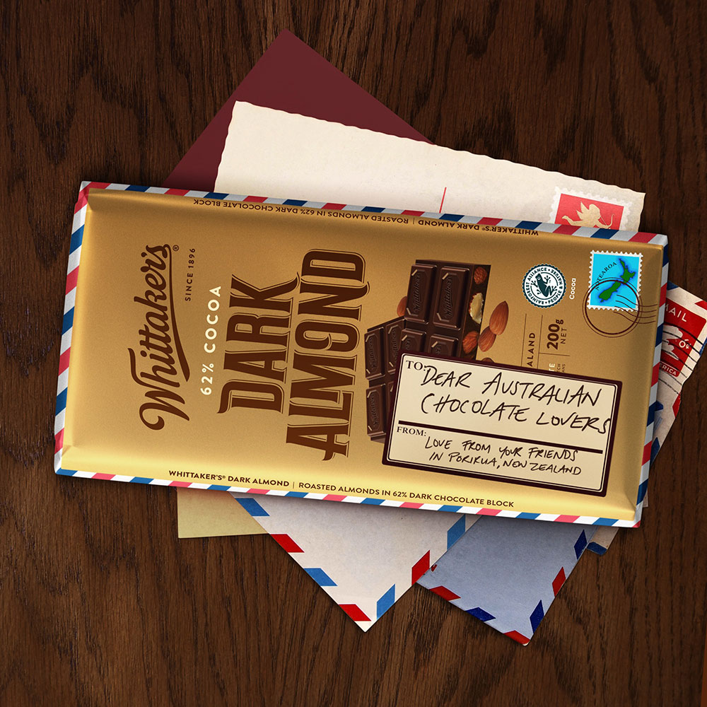 A block of Whittaker's Dark Almond sits on a bench with a note reading, "Dear Australian chocolate lovers, love from your friends in Porirua, New Zealand".