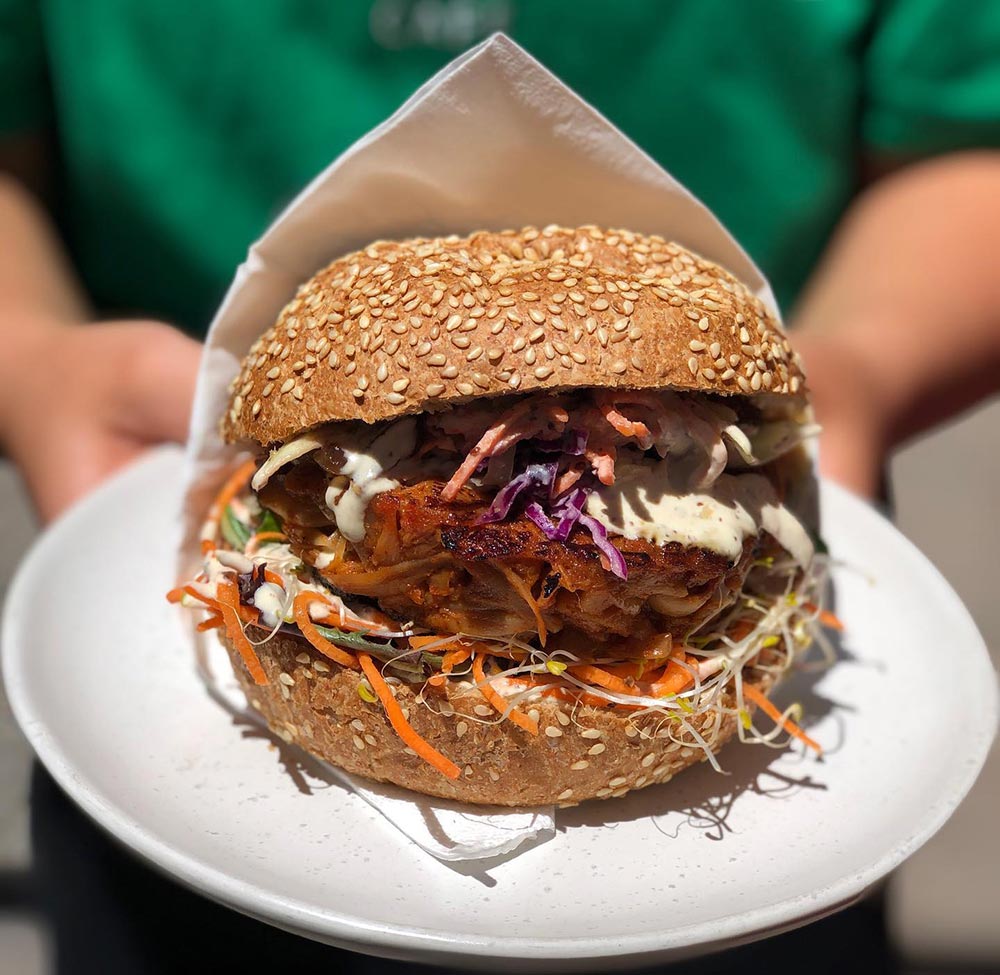 A person holds a vegan burger on a plate.