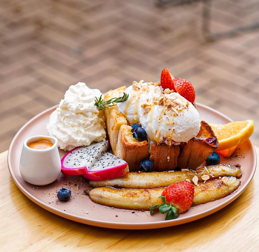 A dessert breakfast topped with ice cream, cream, and a range of fruit. 