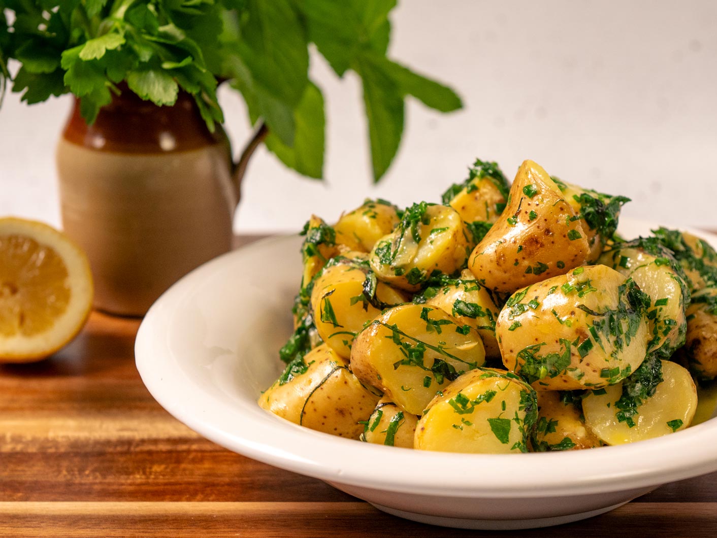 A white bowl on a wooden table, full of buttery looking Irish minted potatoes.