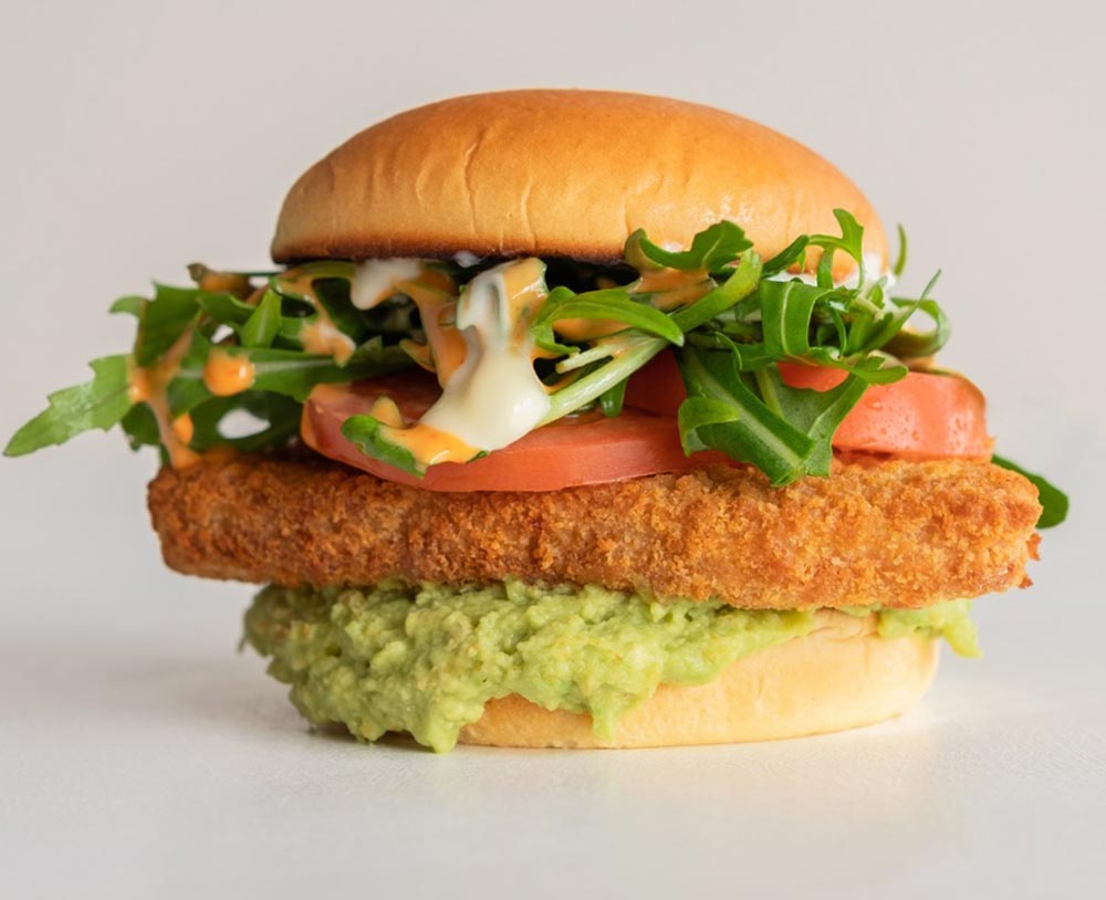 A tall burger using V2 schnitzel sits on a plain white background.