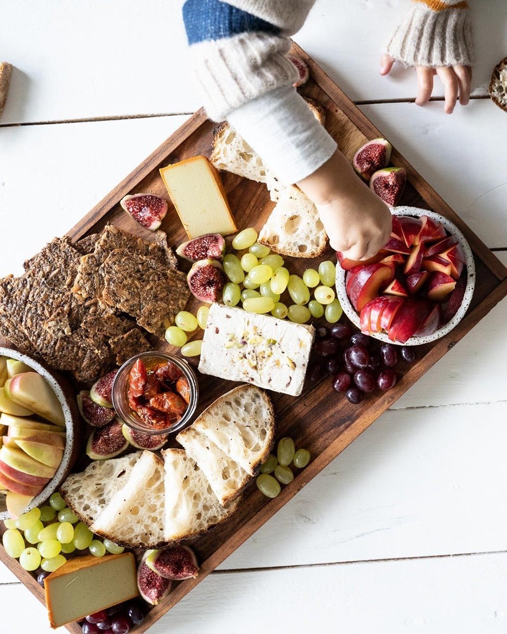 An overhead view of a vegan cheese board complete with crusty bread, crackers, and an assortment of fruits.
