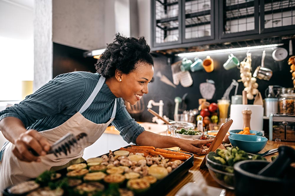 Woman watching recipe in digital tablet while grilling food on electrical barbecue at domestic kitchen.