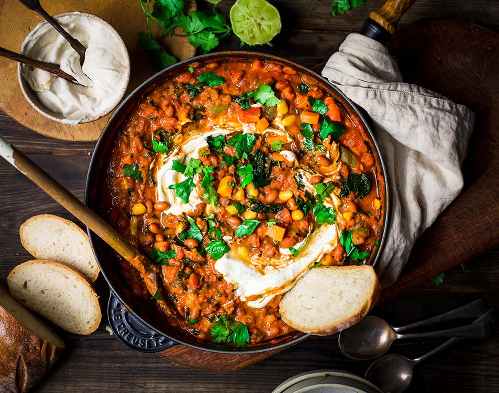 A plant-based diet is rich in nutrients: A skillet of sweet potato and black bean chilli sits on a tea towel on a table, surrounded by slices of crusty bread.