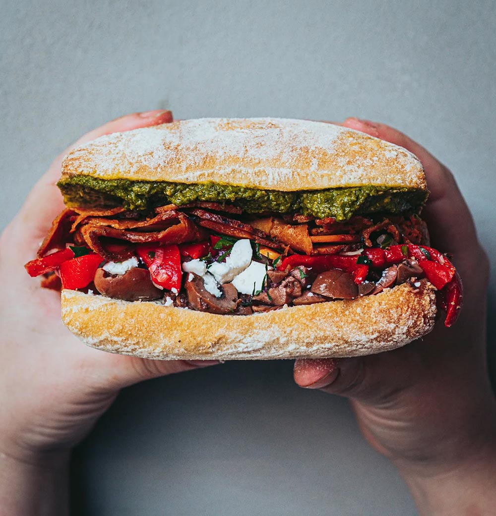 Smith and Deli sandwich: A pair of hands hold up 'the Godfather', a toastie on Turkish bread with layers of spicy salami, pesto, olives, Spanish peppers, feta, and rocket.