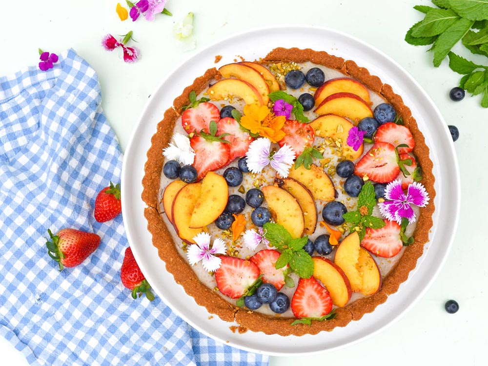 Vegan desserts: Overhead view of the native summer custard tart, decorated with colourful fruits and edible flowers. 