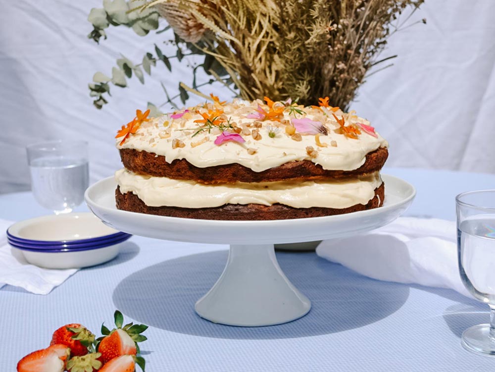 A layered hummingbird cake sits atop a cake stand decorated with edible flowers. 