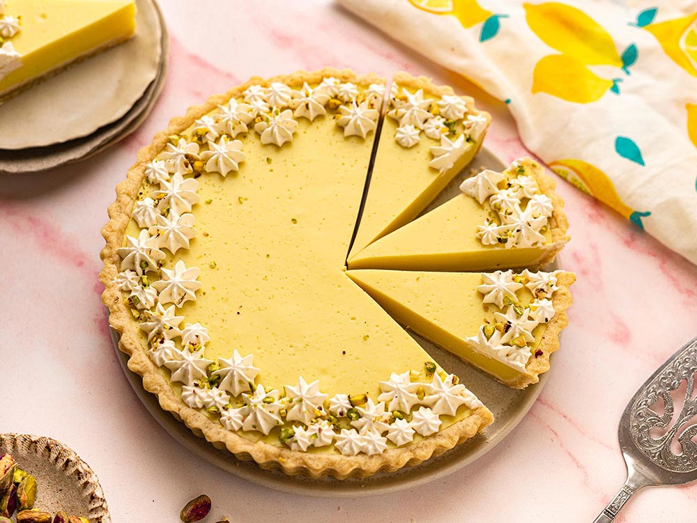 An overhead shot of a beautifully decorated lemon tart, with three slices pre-cut.