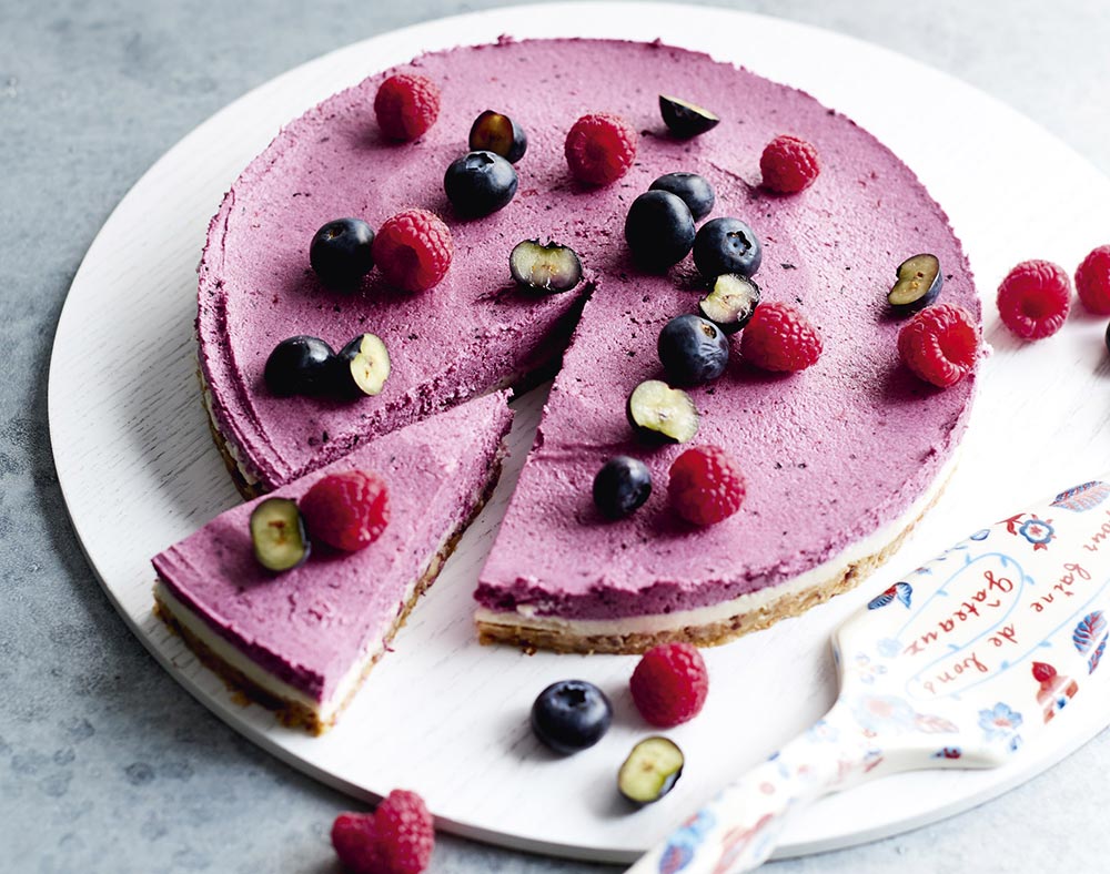 Vegan desserts: A beautiful berry cheesecake in a vibrant purple on a serving tray, topped with various berries. 