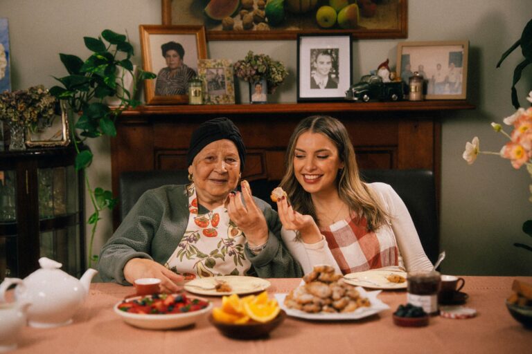 Nanna sitting at her dining table with her granddaughter Claud with a plate of fresh frittole in front of them.