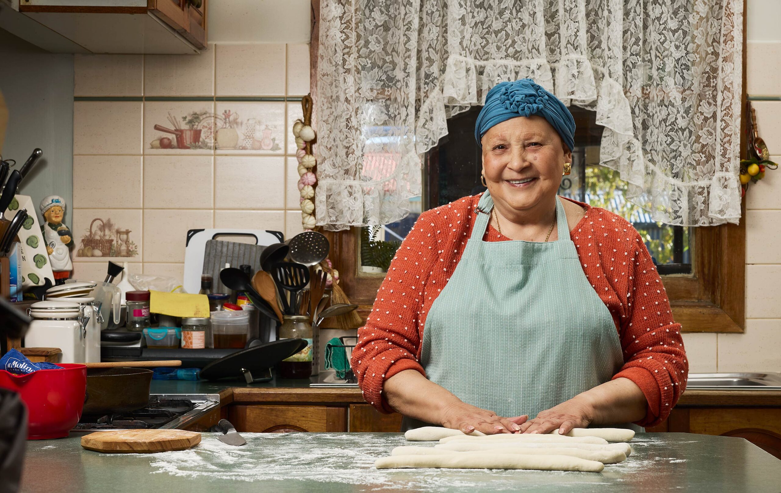 Nanna standing proudly at her kitchen bench rolling gnocchi as she smiles to the camera.