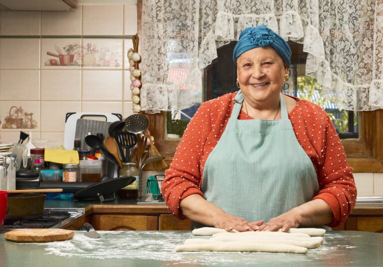 Nanna standing proudly at her kitchen bench rolling gnocchi as she smiles to the camera.