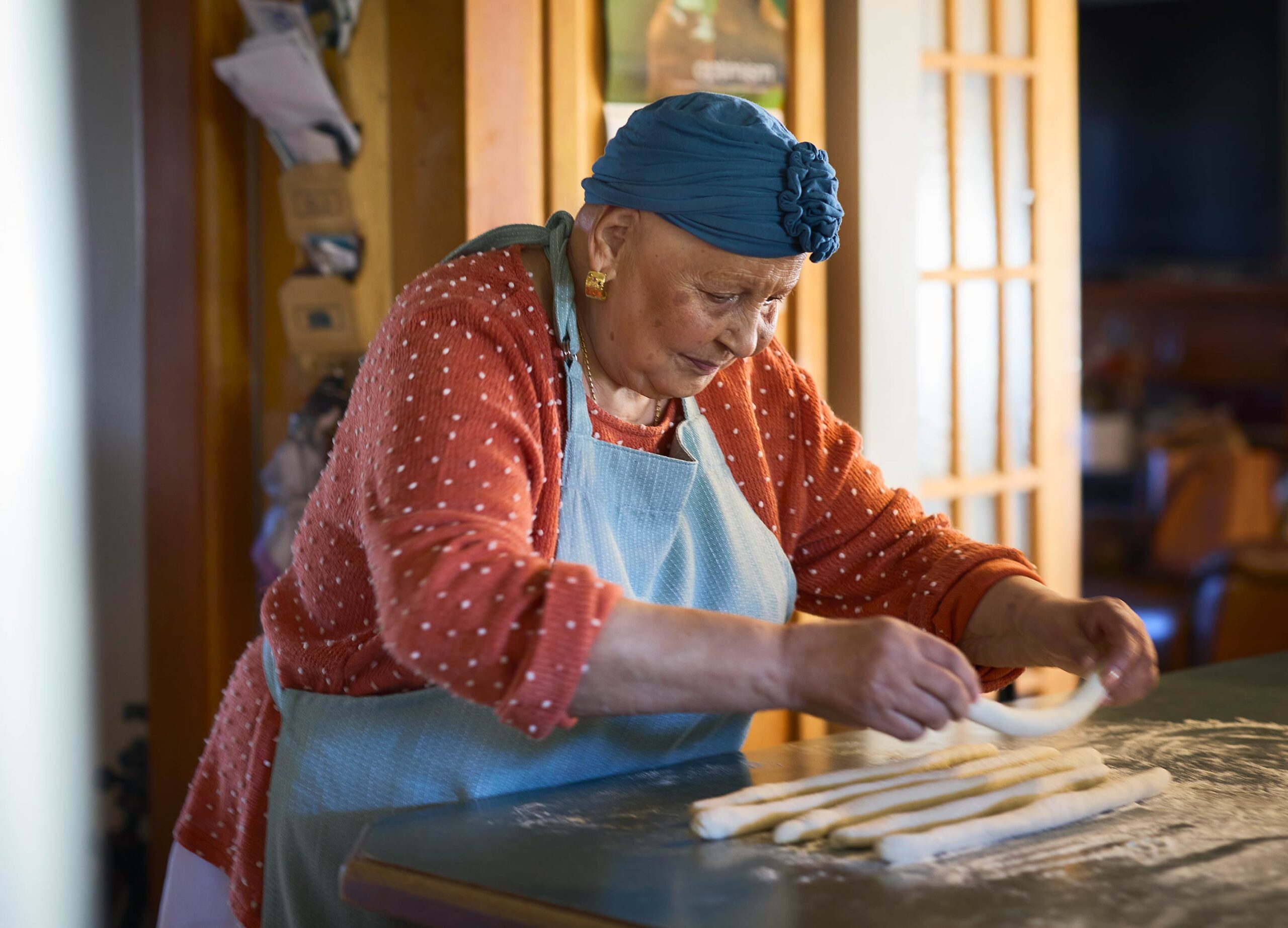 Nanna looking down at the bench focussing on rolling dough to make gnocchi in her kitchen.