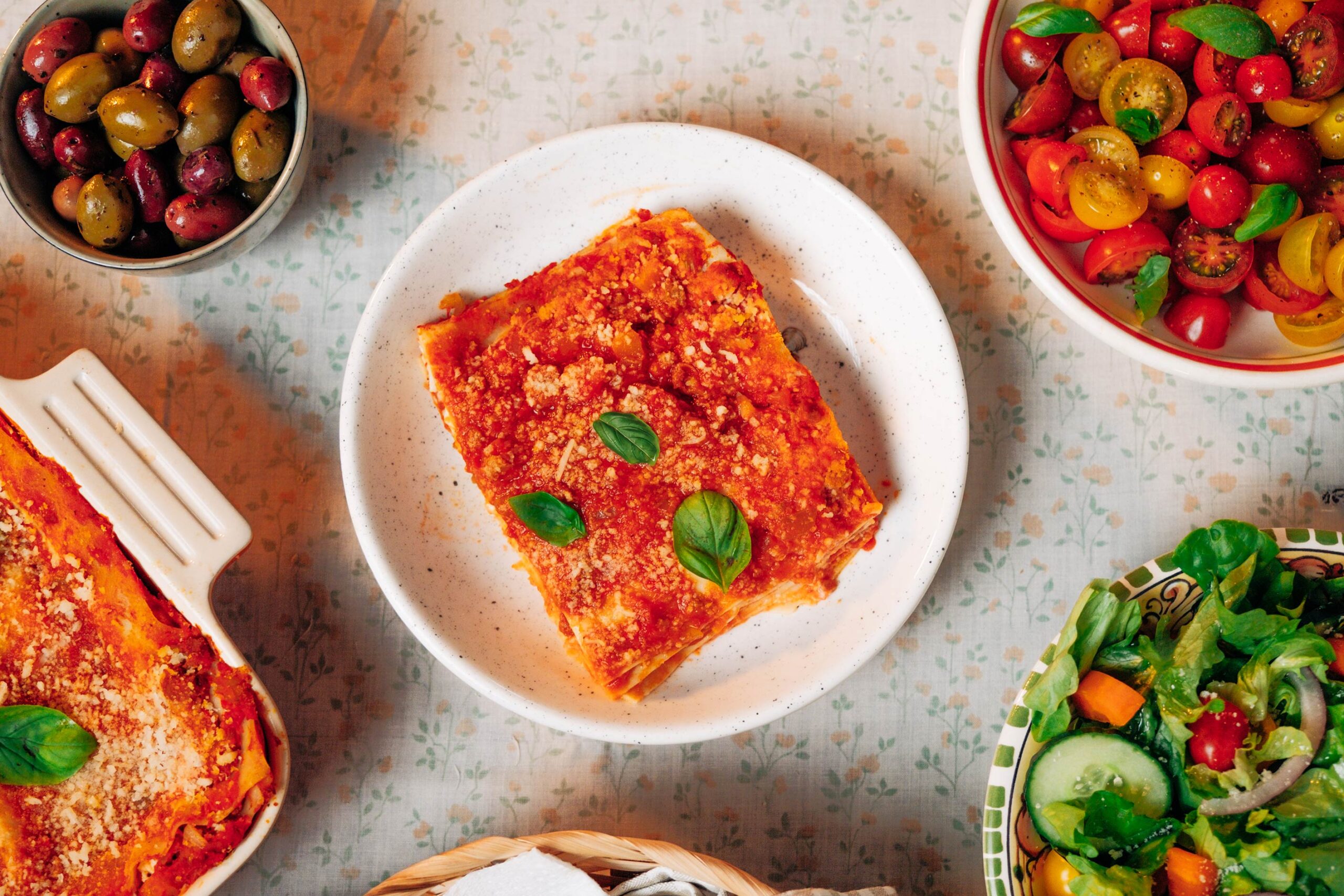 A portion of lasagne on a plate surrounded by dishes of delicious salads as featured in VegKit's "The Nanna Diaries" series.