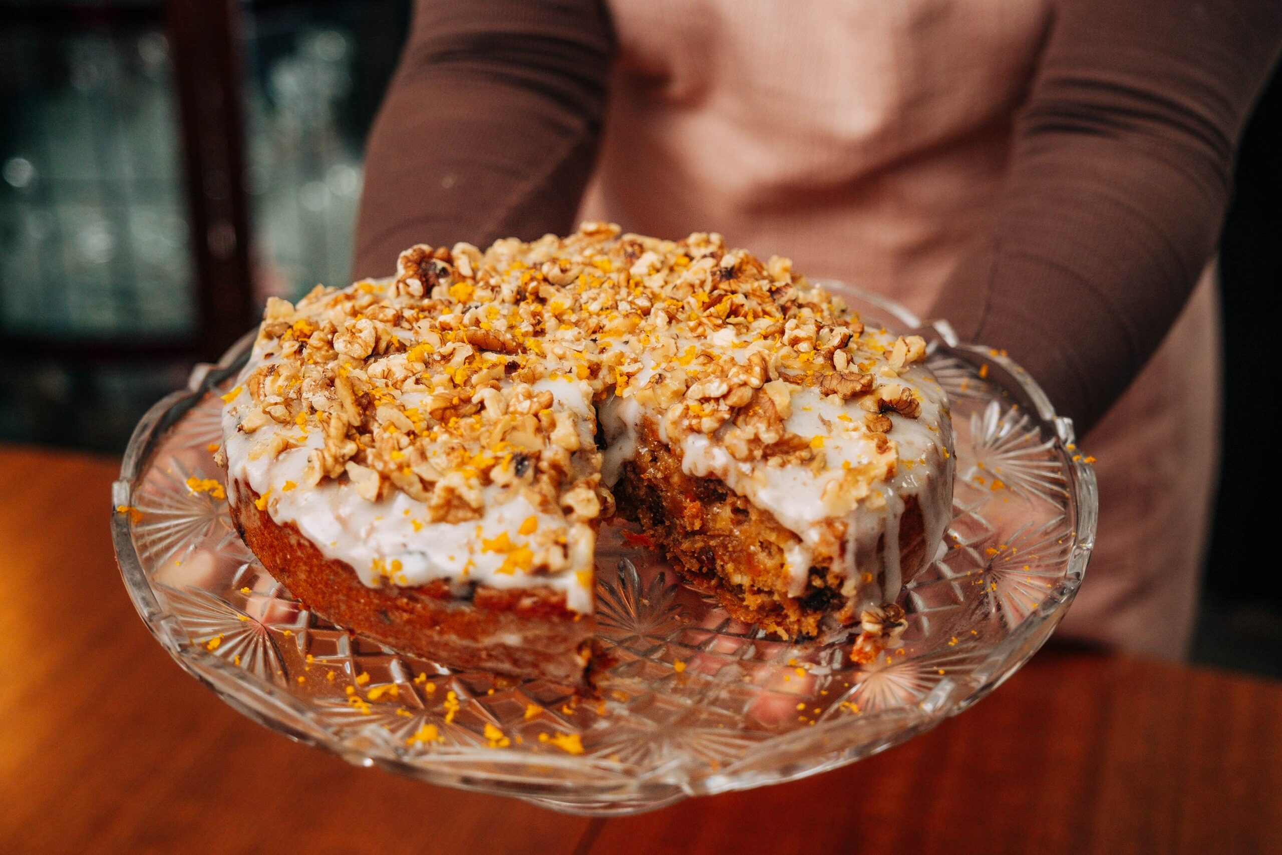 Carrot cake on a crystal plate that is being placed onto the table as featured in VegKit's "The Nanna Diaries" series.
