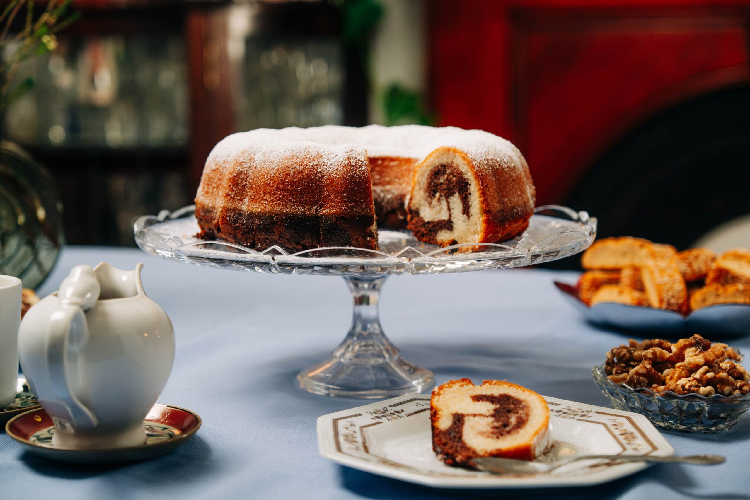 Marble cake on a crystal cake stand on a table with tea and other goodies as featured in VegKit's "The Nanna Diaries" series.