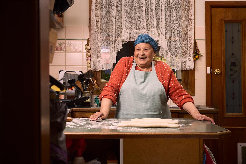 Nanna Mirella in her kitchen in her apron, looking happy.