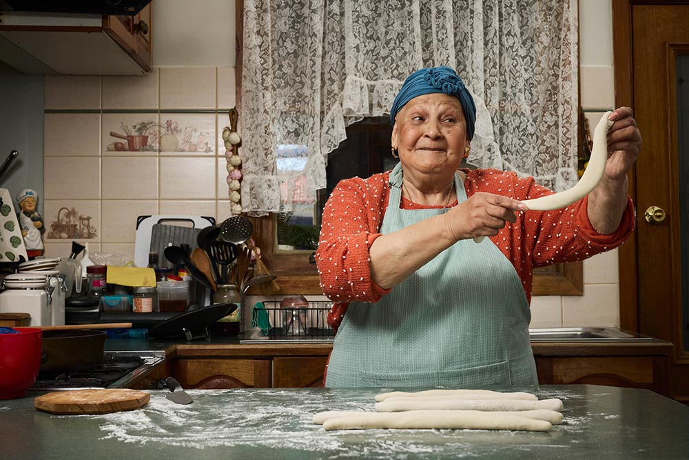 Mirella in the kitchen holding a length of dough, looking cheeky!