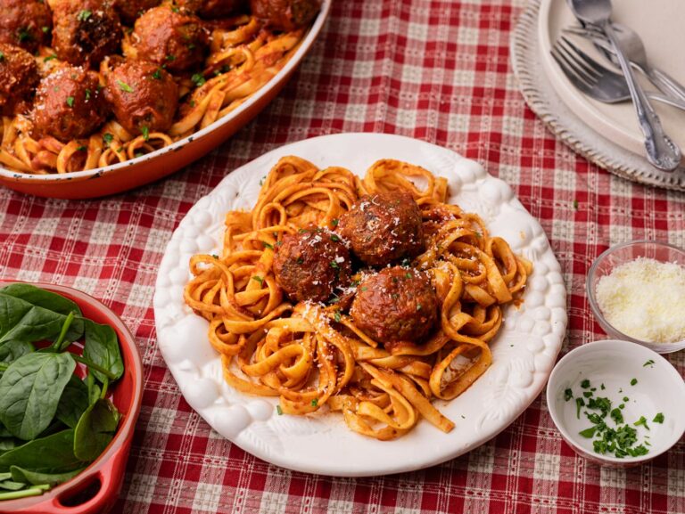 Fettucine with meatballs in Napoli sauce served on a white plate with a red and white checked tablecloth