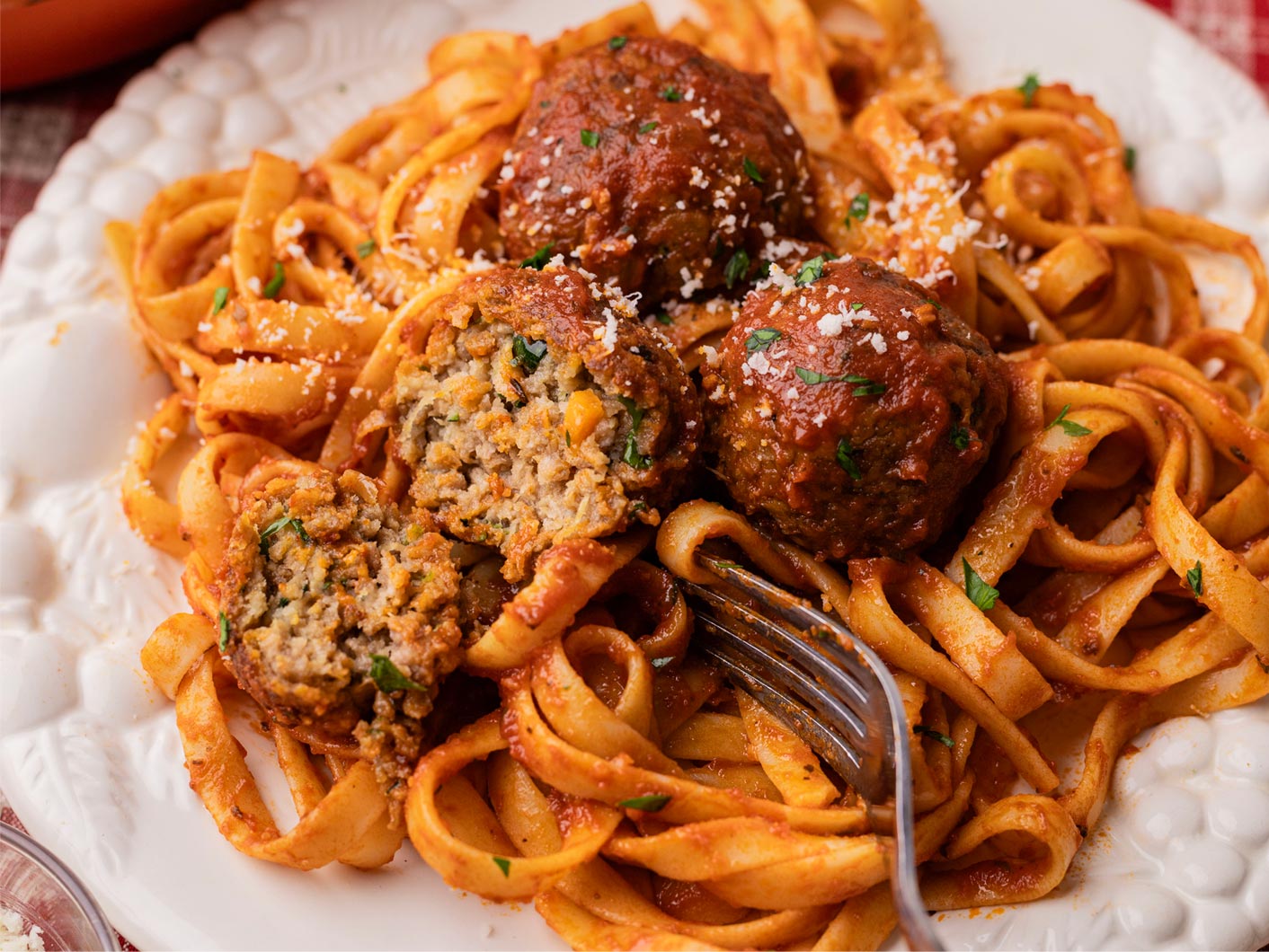 Fettucine with meatballs in Napoli sauce served on a white plate. One meatball has been cut to reveal the centre,