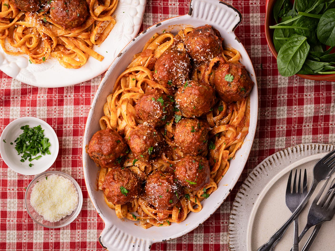 Fettucine with meatballs in Napoli sauce served in a white serving dish with a red and white checked tablecloth
