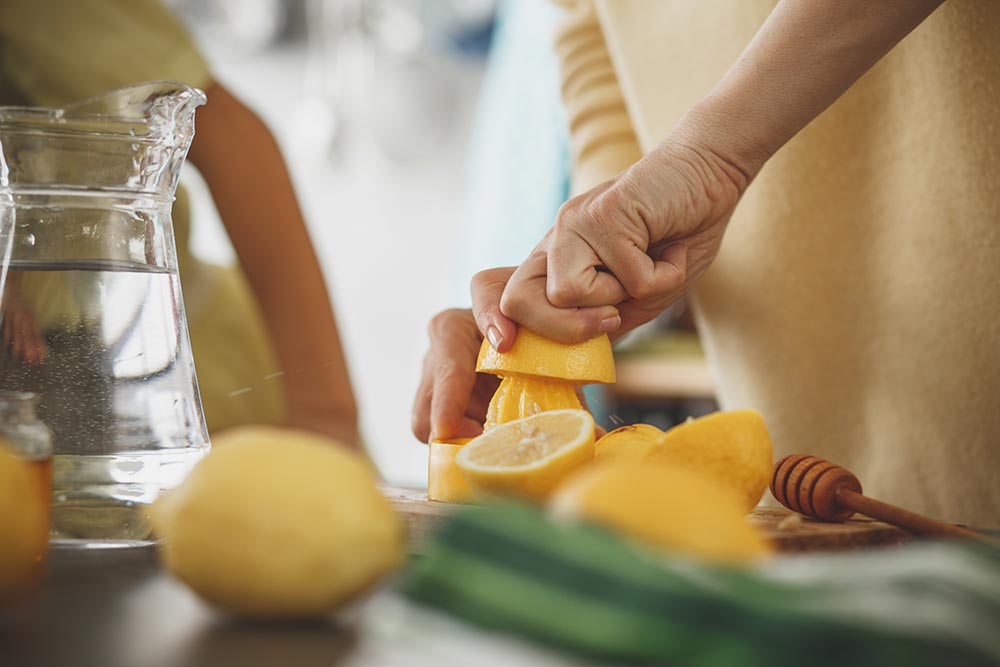 A person in squeezing lemons on a kitchen bench. 