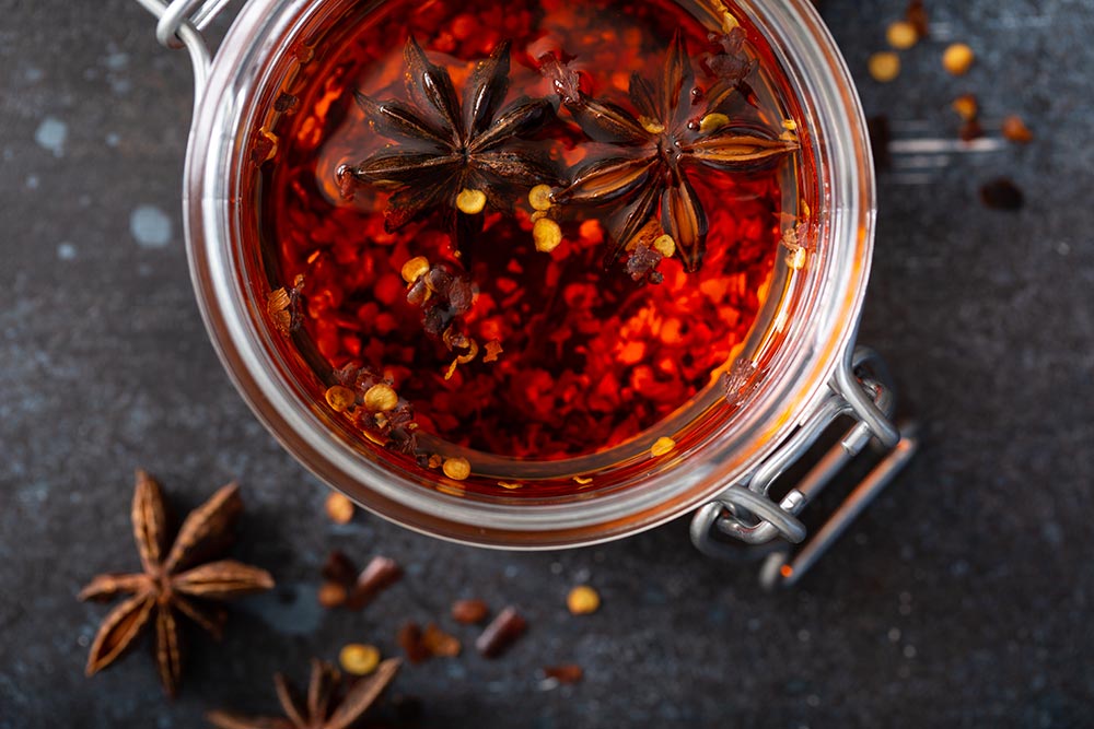 An overhead image of a glass storage jar filled with crispy chilli oil. Star anise floats on the top, infusing its flavour. 