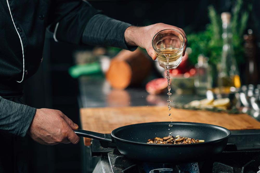 A person pours a glass or red wine over mushrooms in a frypan. 