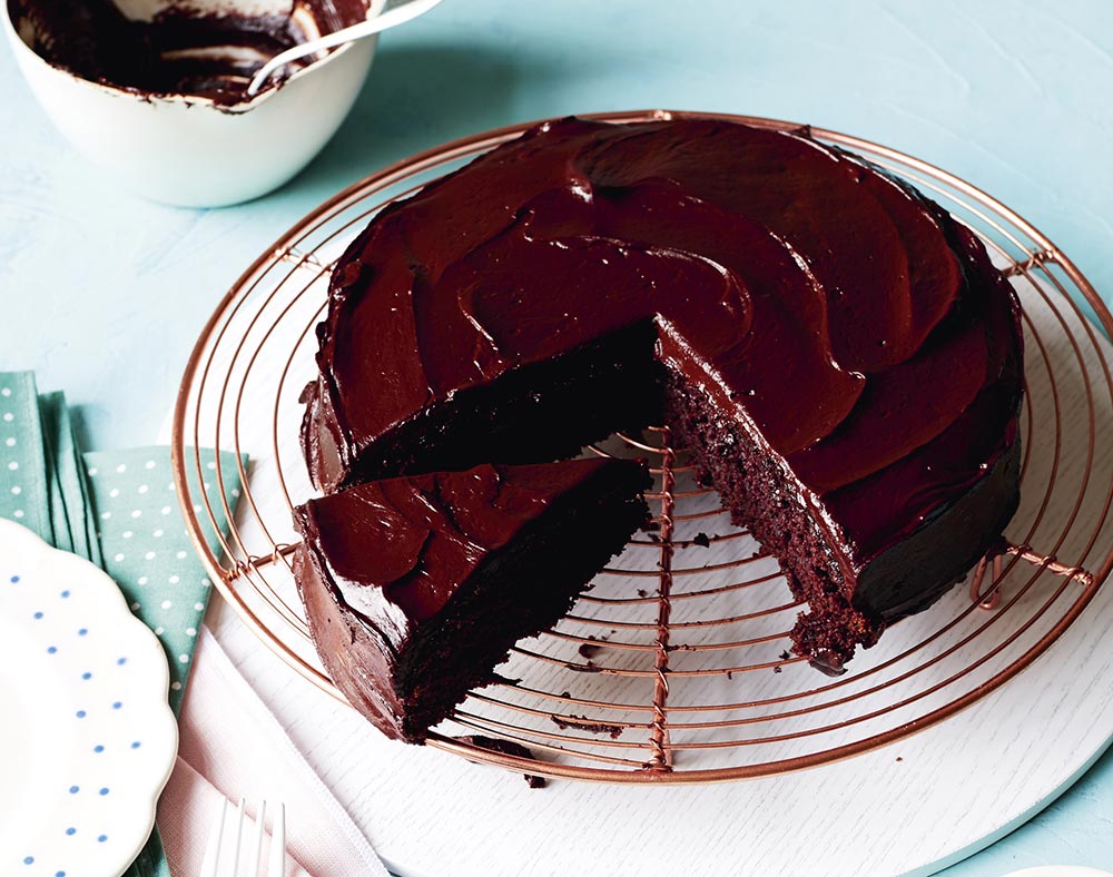 A rich, fudgy chocolate cake sits on a cooling rack, topped with a decadent ganache.