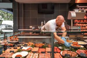 A butcher is packaging red meat from a full deli counter.