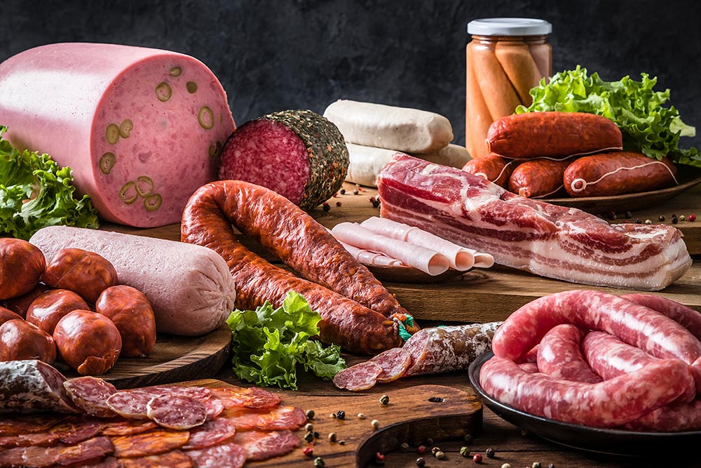 Front view of various kinds of raw sausages like mortadella, bacon, salami, ham and pickled sausages in a delicatessen.