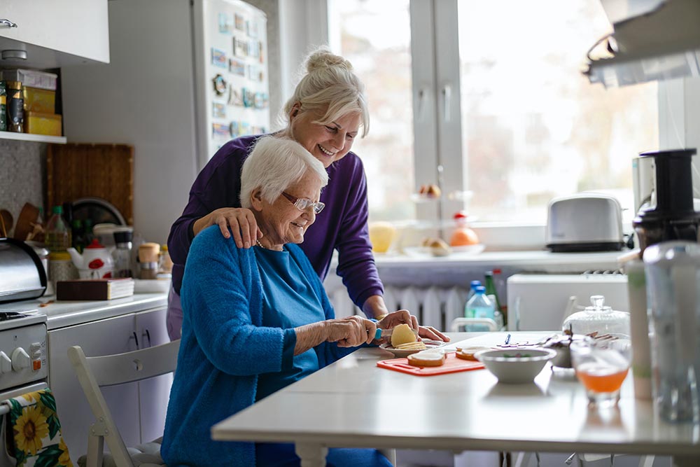 A woman visits her elderly mother in her home, who is preparing food. 