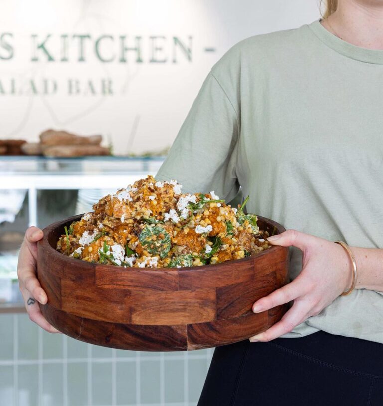 An employee holds a giant wooden salad bowl full of vegan cous cous salad.