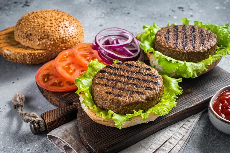 Plant based meatless burgers with vegan grilled pattie, tomato and onion on a wooden serving board.