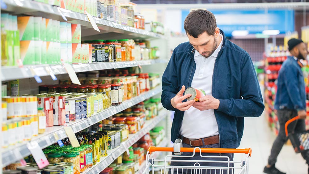 A man in the supermarket is checking the nutritional information on the back of a tinned product – study shows vegan diet leads to weight loss (even with processed foods)