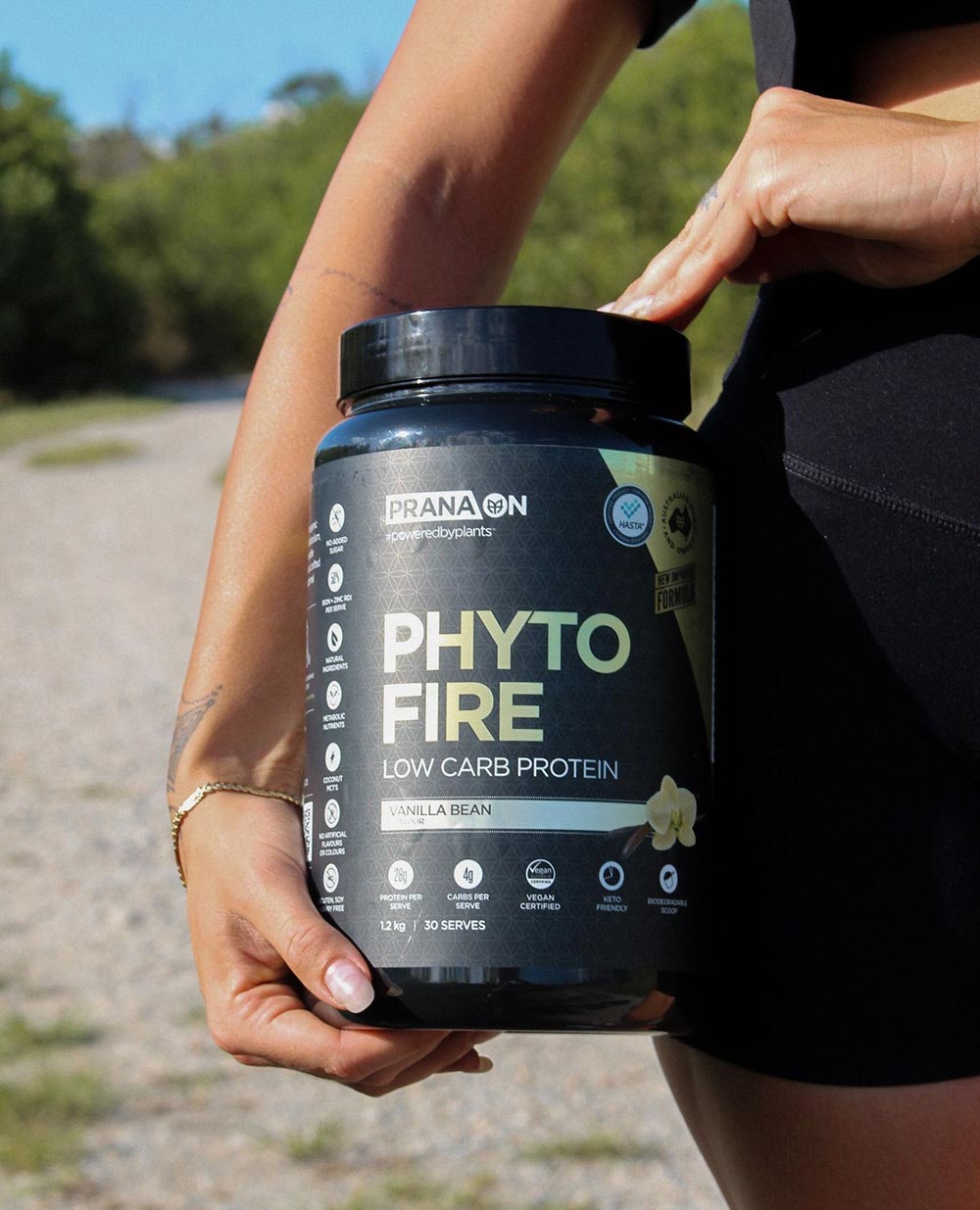 A person stands outside holding a large container of PranaOn protein powder to their side.