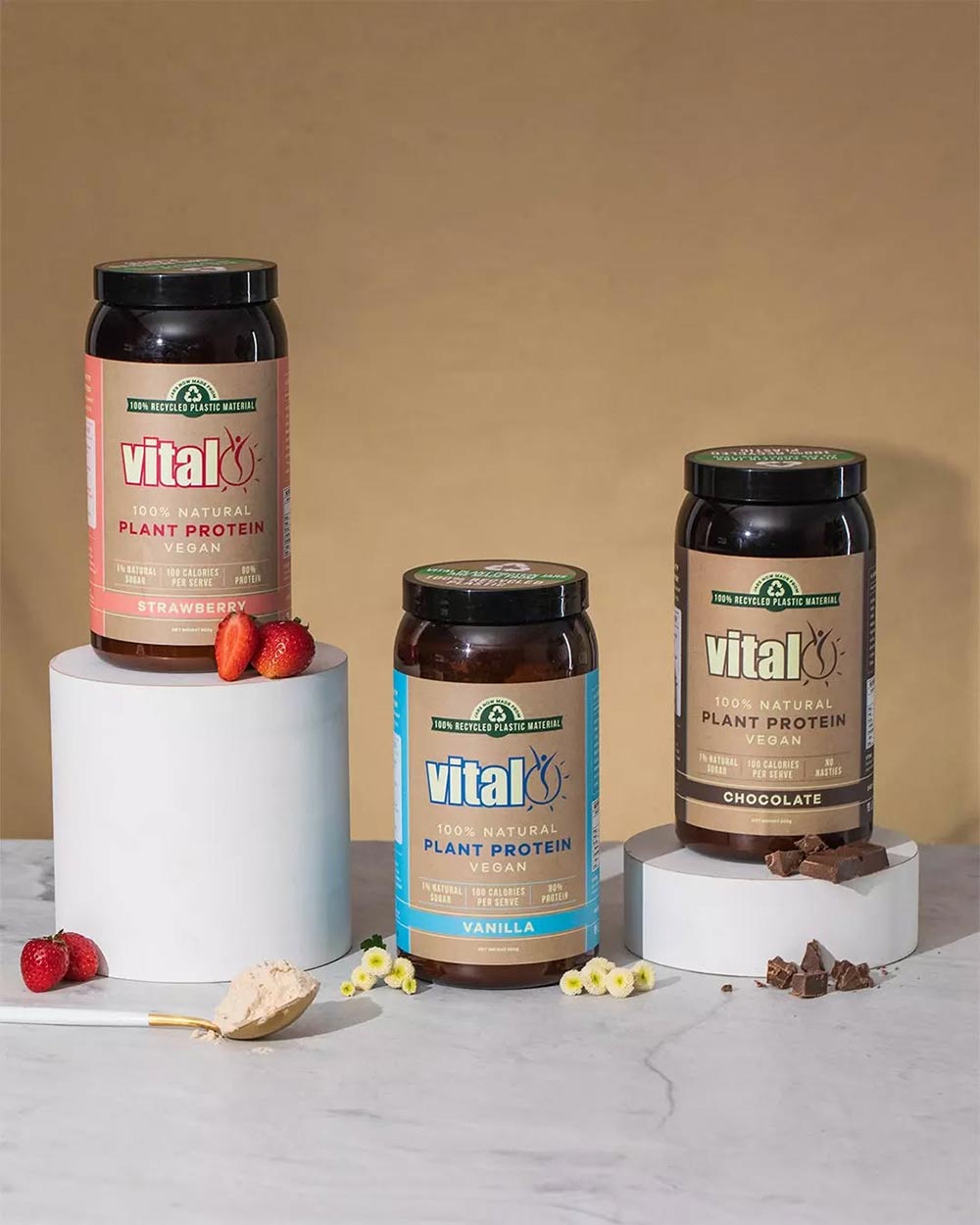 Three different flavours of Vital plant protein sit on differing size plinths on a light brown background.