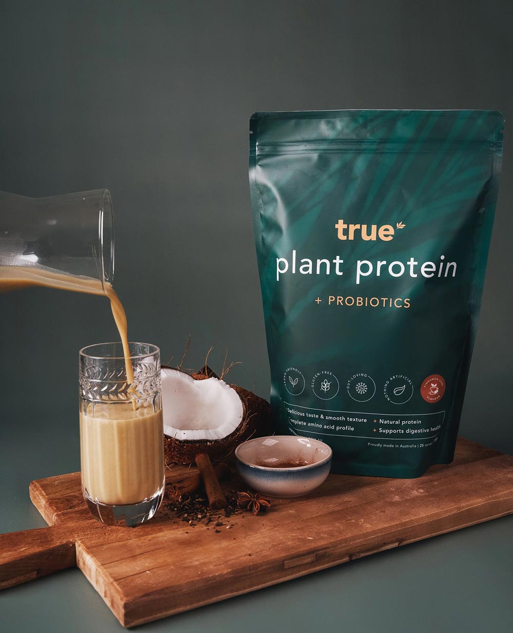 A pack of True Protein plant protein sits on a wooden chopping board as a smoothie is being poured next to it. 